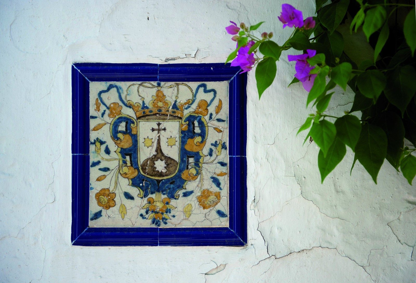 Azulejo sevillano con el escudo del Carmelo, enmarcado en azul, junto a una buganvilla