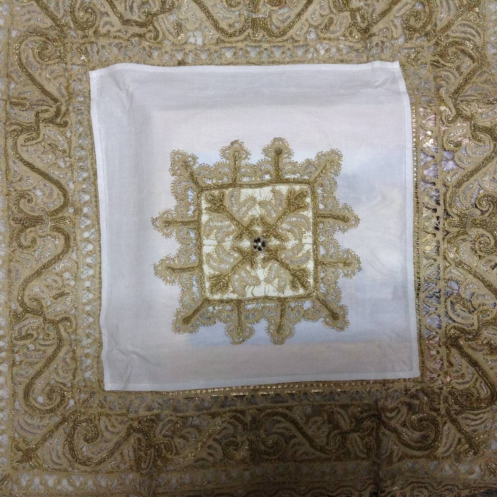 Paño blanco con una cenefa ancha y un cuadro central de volutas bordados en hilo de oro