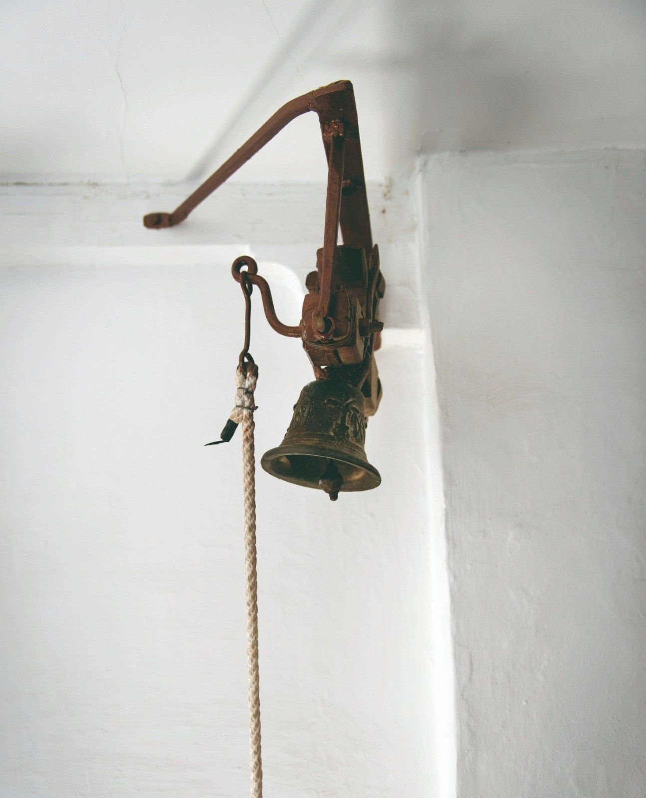 Pequeña campana de bronce colgada de un soporte de hierro en una pared blanca
