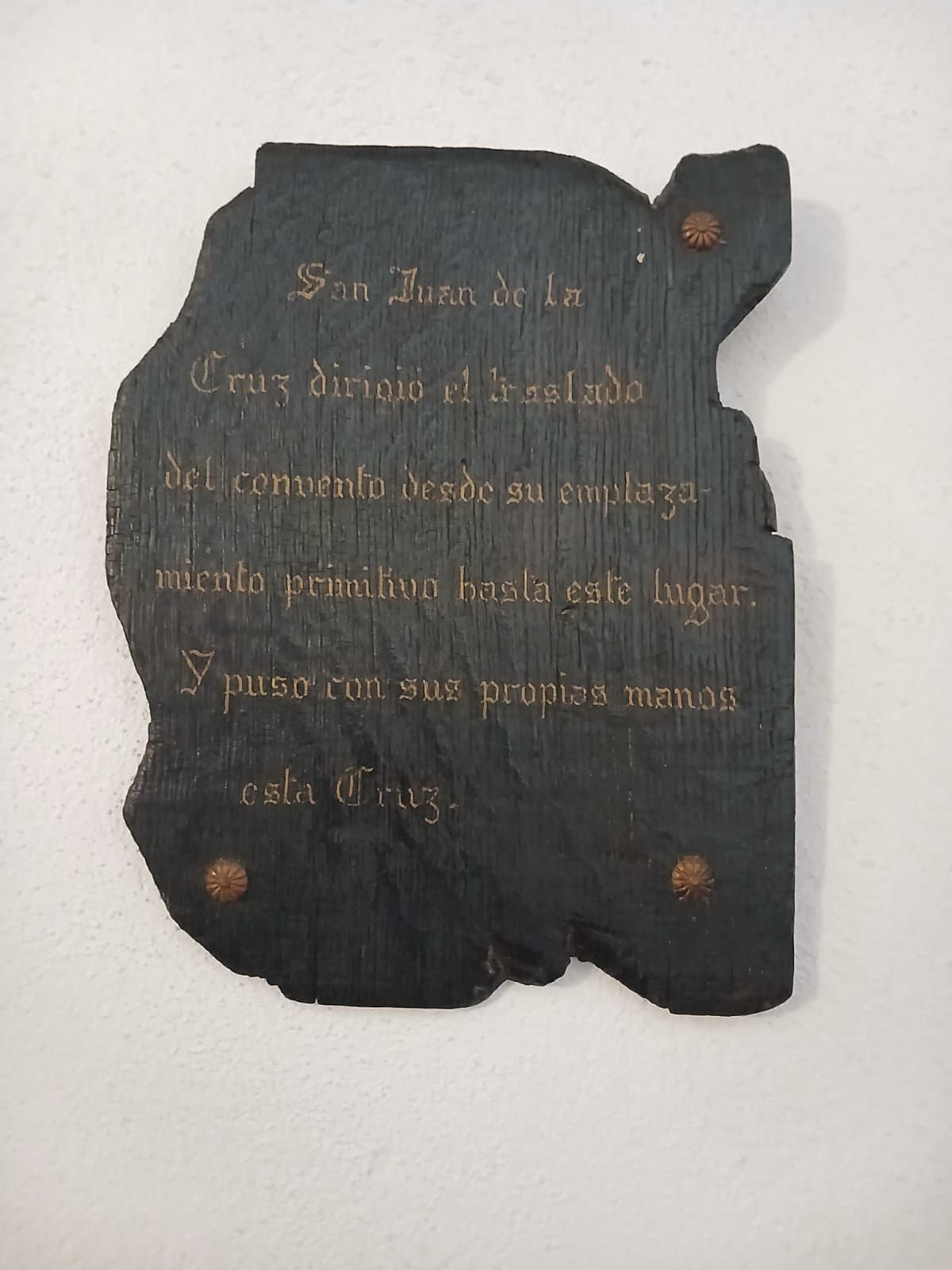 Lápida de madera oscura con letras doradas sobre San Juan de la Cruz y el traslado del convento