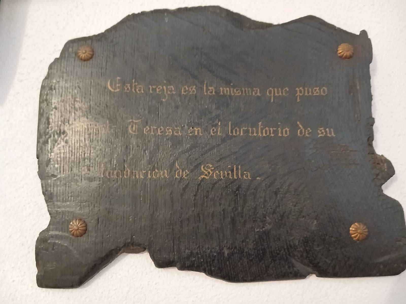 Lápida de madera oscura con letras doradas: Esta reja es la misma que puso Teresa en el locutorio de su fundación de Sevilla