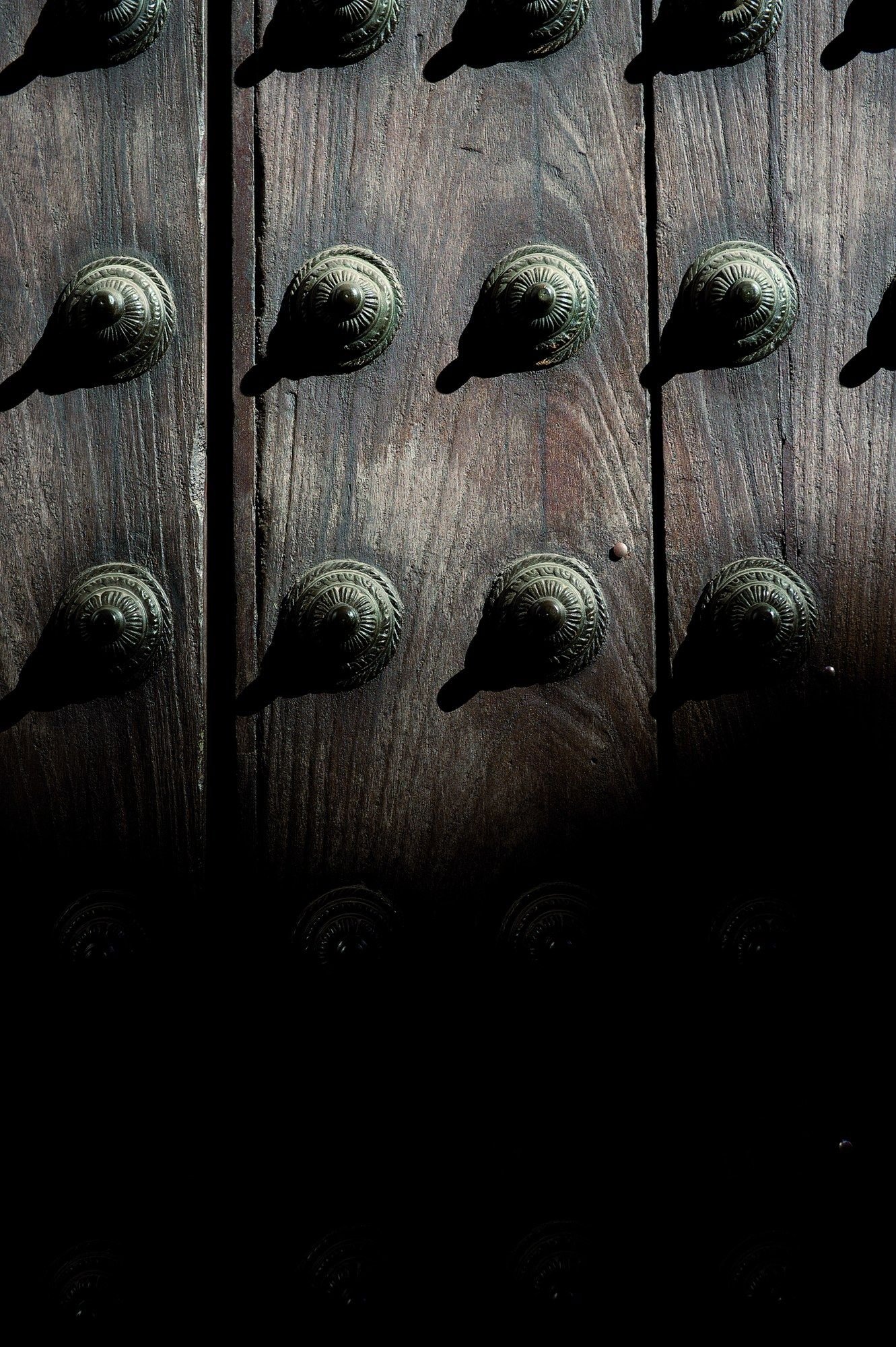 Detalle de los clavos de hierro de una puerta de madera, en penumbra