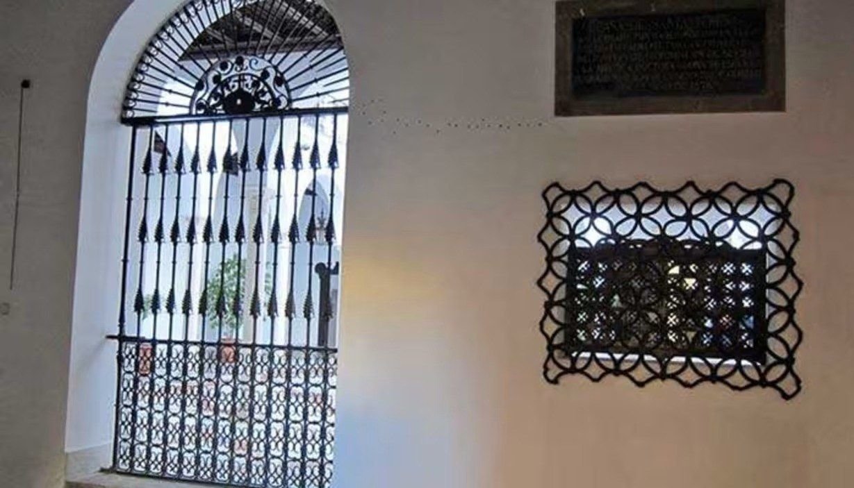 Ventana de medio punto con reja de forja y una celosía de hierro en un muro blanco